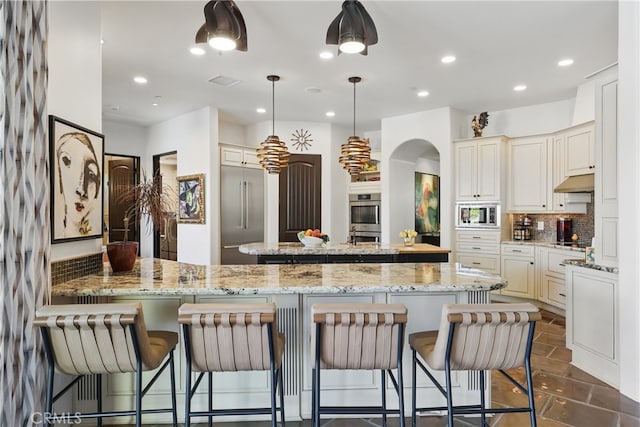 kitchen with a center island, tasteful backsplash, built in appliances, arched walkways, and visible vents