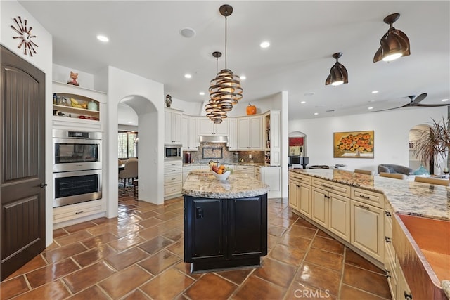 kitchen featuring cream cabinetry, stainless steel appliances, backsplash, arched walkways, and a center island