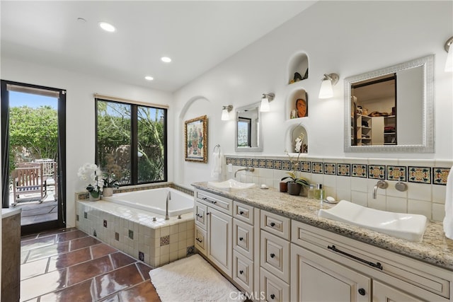 bathroom featuring a bath, a sink, double vanity, tasteful backsplash, and recessed lighting