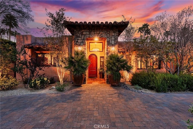 mediterranean / spanish-style house featuring a tile roof, stone siding, and stucco siding