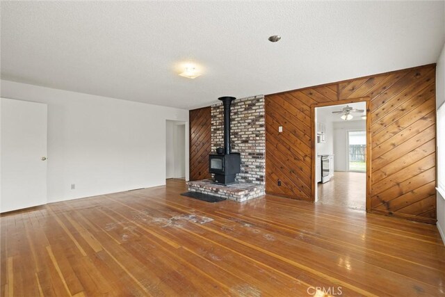 2909 Carlene Pl, Chico, CA 95973 - unfurnished living room featuring a wood stove, wood-type flooring, wooden walls, a ceiling fan, and a textured ceiling