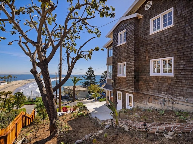 view of property exterior featuring a patio, a beach view, a water view, and fence