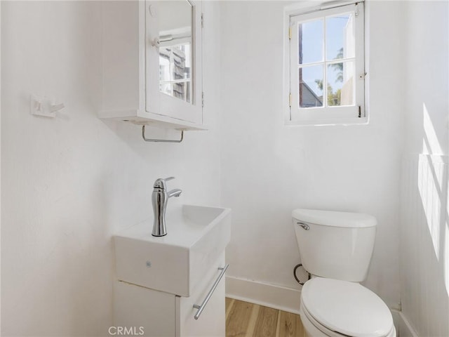 half bathroom with toilet, vanity, wood finished floors, and baseboards
