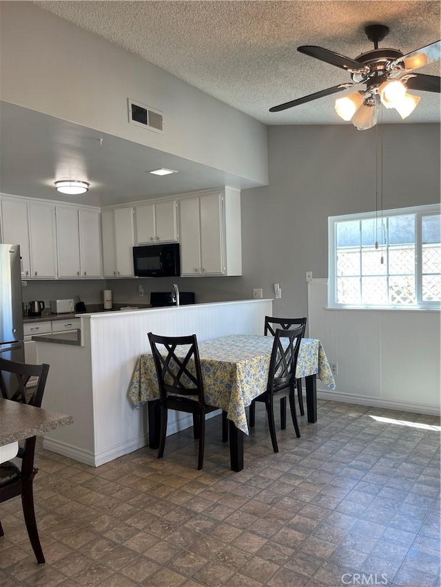 7320 Ramona Ave, Rancho Cucamonga, CA 91730 - kitchen featuring black microwave, ceiling fan, freestanding refrigerator, white cabinets, and a textured ceiling