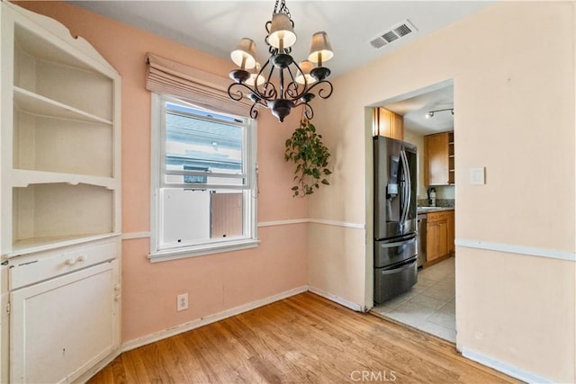 unfurnished dining area with visible vents, baseboards, a chandelier, light wood-type flooring, and a sink