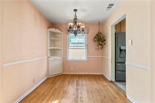 unfurnished dining area with a notable chandelier, light wood-style flooring, baseboards, and visible vents