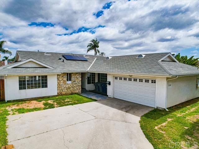 single story home with stone siding, a garage, stucco siding, roof mounted solar panels, and concrete driveway
