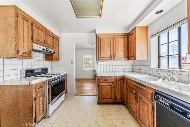 kitchen featuring white gas stove, light floors, under cabinet range hood, dishwasher, and a sink