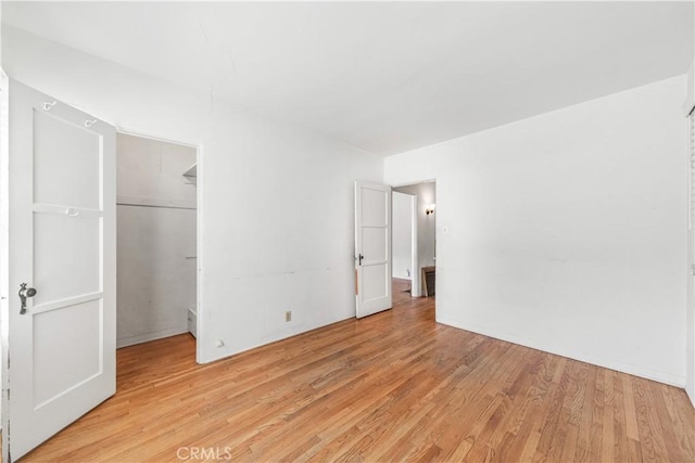 unfurnished bedroom featuring a closet, light wood finished floors, and a walk in closet