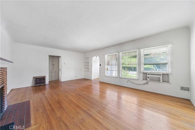 unfurnished living room with arched walkways, a brick fireplace, heating unit, and wood finished floors