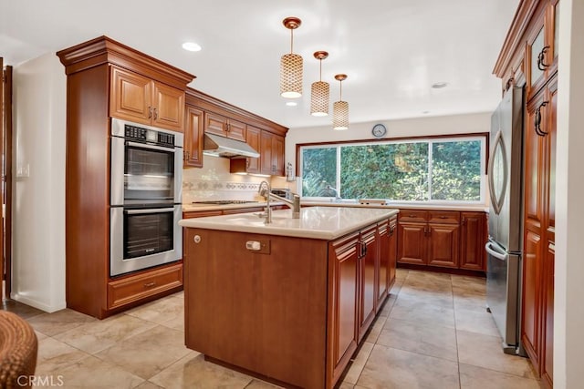 kitchen featuring recessed lighting, light countertops, under cabinet range hood, a center island with sink, and appliances with stainless steel finishes