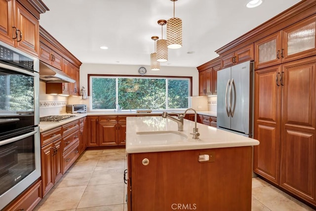 kitchen featuring a sink, light countertops, appliances with stainless steel finishes, under cabinet range hood, and brown cabinetry