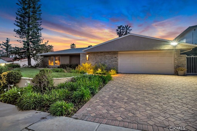 view of front of home with decorative driveway, stone siding, a garage, and stucco siding