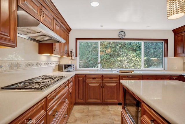 kitchen featuring black microwave, tasteful backsplash, stainless steel gas stovetop, under cabinet range hood, and a sink