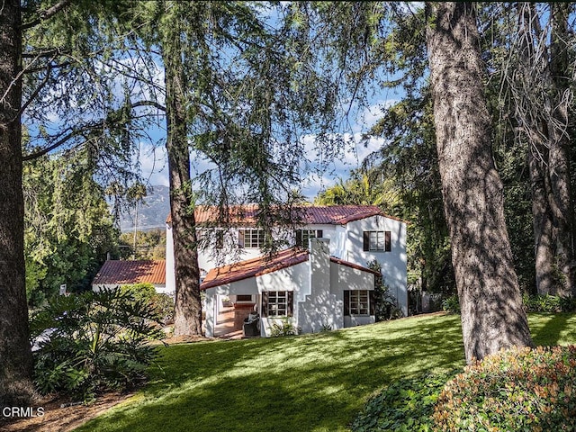 rear view of house featuring a lawn, a tiled roof, and stucco siding