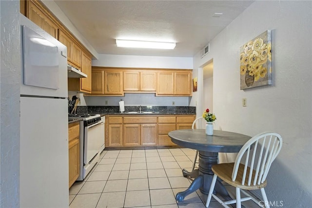 609 Rancheria Dr, Chico, CA 95926 - kitchen with white appliances, under cabinet range hood, dark countertops, and light tile patterned floors