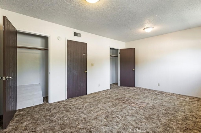 unfurnished bedroom with a textured ceiling, two closets, visible vents, and carpet floors