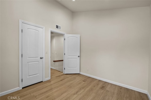 interior space with a towering ceiling, baseboards, visible vents, and light wood-type flooring