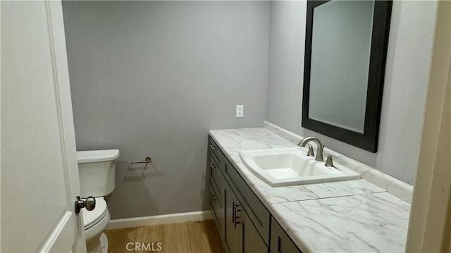 half bathroom featuring toilet, baseboards, wood finished floors, and vanity
