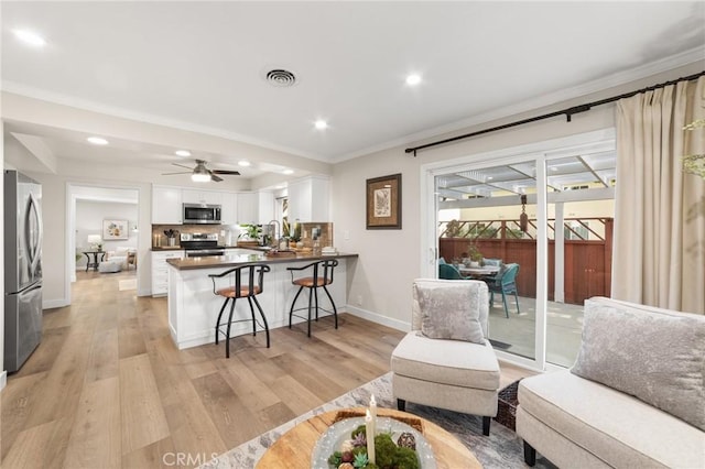 living area featuring visible vents, a ceiling fan, ornamental molding, and light wood-style flooring