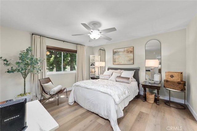 bedroom with arched walkways, light wood finished floors, and baseboards