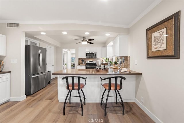 kitchen with visible vents, white cabinets, appliances with stainless steel finishes, light wood-style floors, and a peninsula