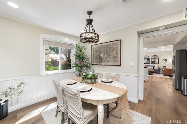 dining area featuring ornamental molding, wood-type flooring, and a wainscoted wall