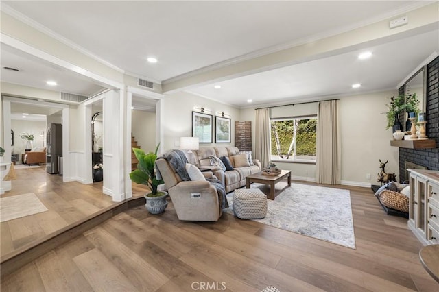 living room with light wood-style floors, crown molding, and visible vents