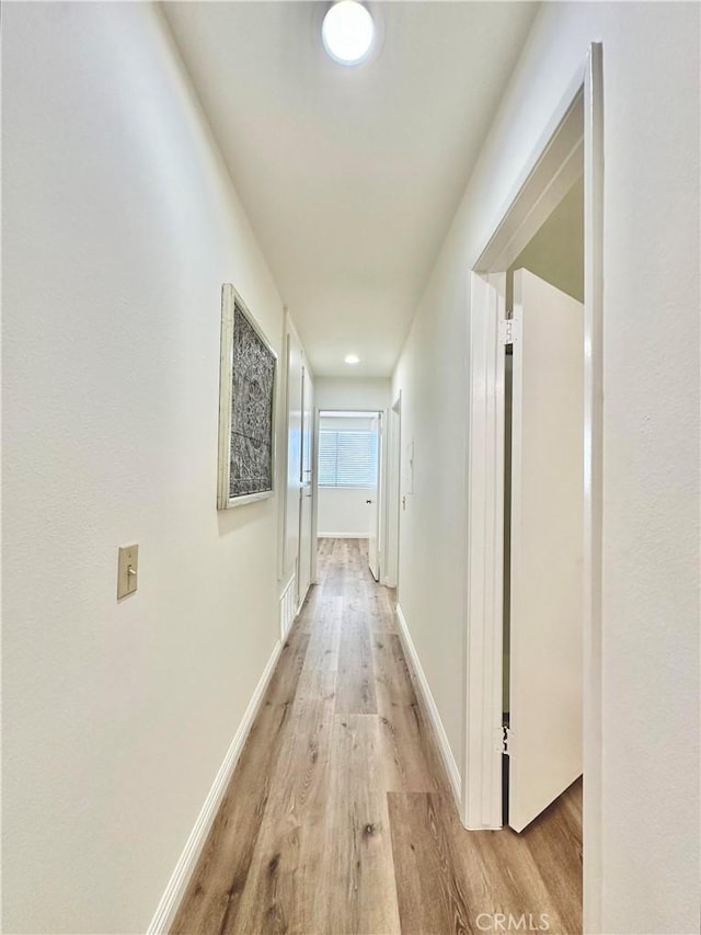 corridor featuring baseboards, light wood-style floors, and visible vents