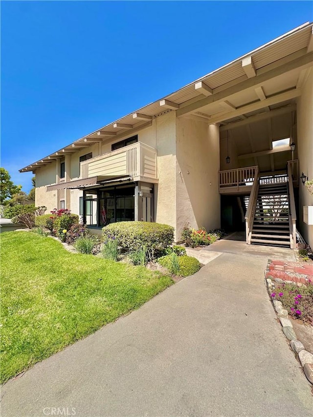 exterior space with stucco siding, stairs, and a lawn