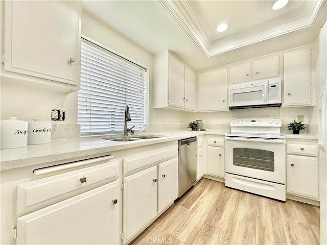 kitchen featuring crown molding, white appliances, a raised ceiling, a sink, and light wood-style floors