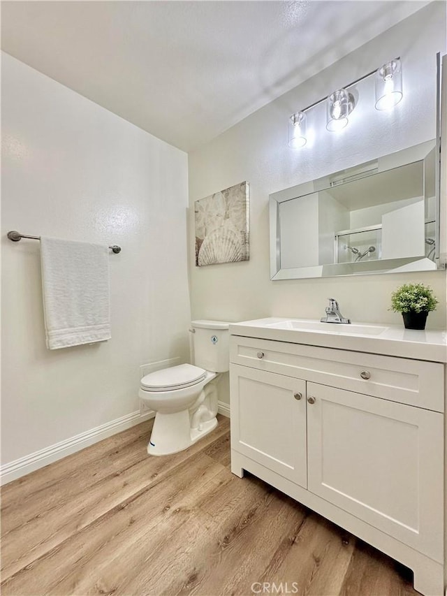 bathroom featuring toilet, vanity, baseboards, and wood finished floors