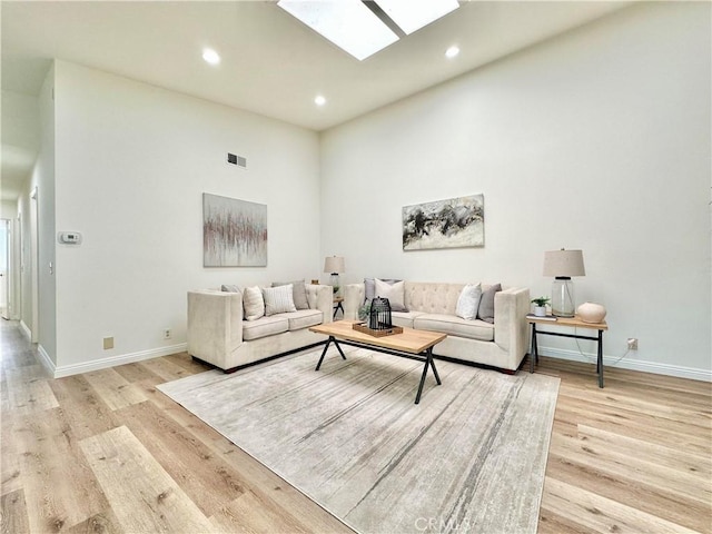 living room featuring baseboards, visible vents, light wood-style floors, and a skylight