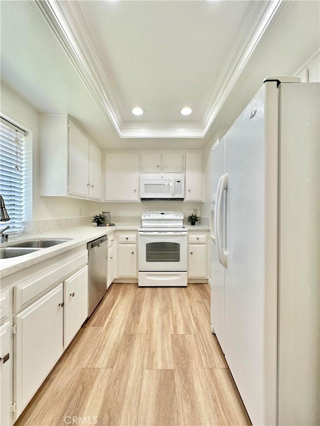 kitchen with a sink, a raised ceiling, light wood-style flooring, white appliances, and ornamental molding