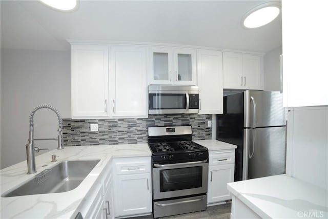 kitchen with a sink, white cabinets, backsplash, and stainless steel appliances