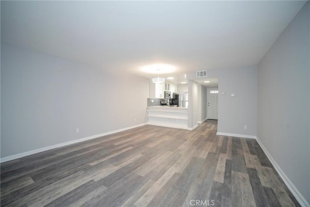 unfurnished living room featuring dark wood-type flooring, baseboards, and visible vents