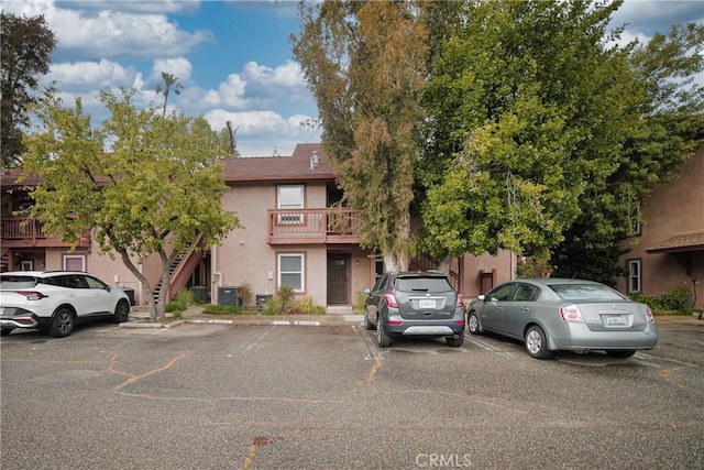 multi unit property featuring stucco siding, central AC unit, uncovered parking, and stairs