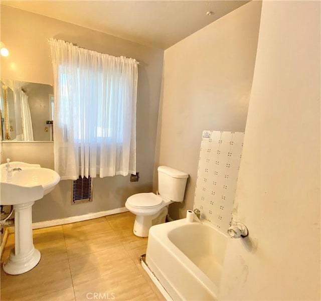 bathroom featuring toilet, tile patterned flooring, a bath, baseboards, and visible vents