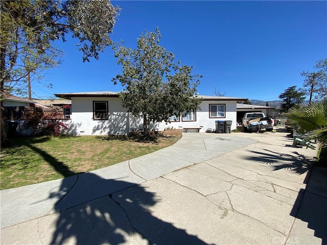 view of front of home featuring driveway, stucco siding, fence, and a front lawn