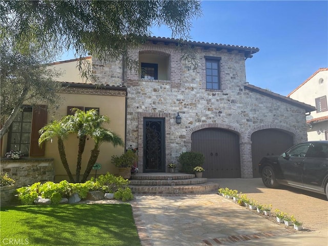 mediterranean / spanish-style home featuring driveway, stucco siding, and stone siding