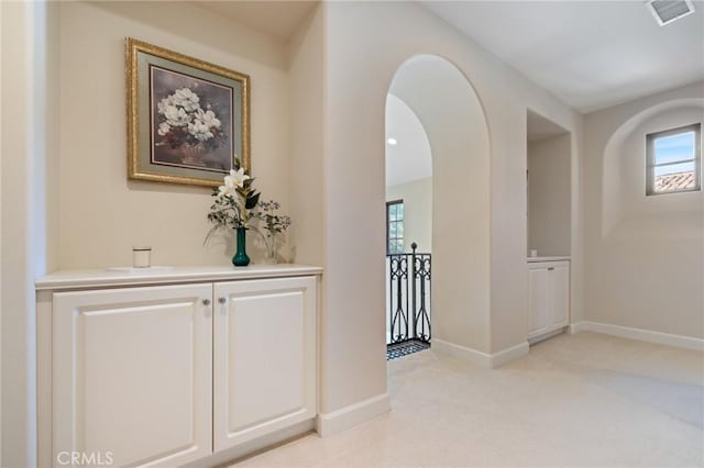 hall featuring arched walkways, light colored carpet, baseboards, and visible vents