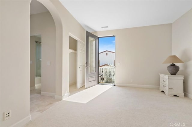carpeted empty room featuring baseboards and arched walkways