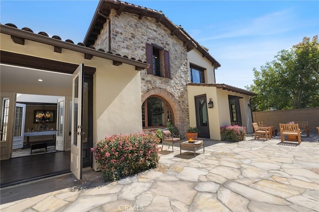 back of house featuring a patio area, fence, stone siding, and stucco siding