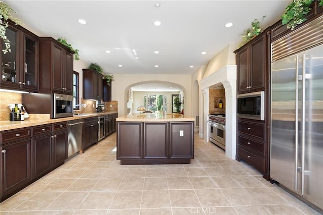 kitchen with light tile patterned floors, arched walkways, recessed lighting, decorative backsplash, and built in appliances