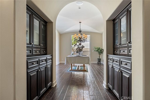 hall with an inviting chandelier, baseboards, dark wood-style floors, and vaulted ceiling