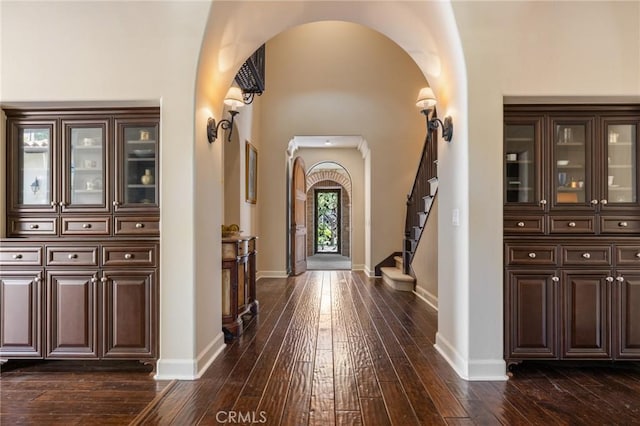 entryway with arched walkways, baseboards, and dark wood finished floors