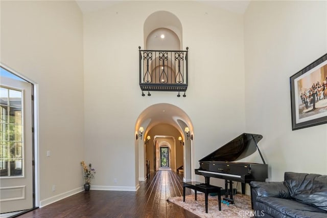 interior space featuring arched walkways, a high ceiling, baseboards, and wood finished floors
