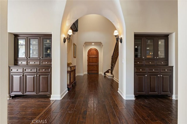 hallway with arched walkways, stairway, dark wood-style flooring, and baseboards