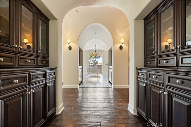 corridor with arched walkways, a notable chandelier, dark wood-style floors, and baseboards
