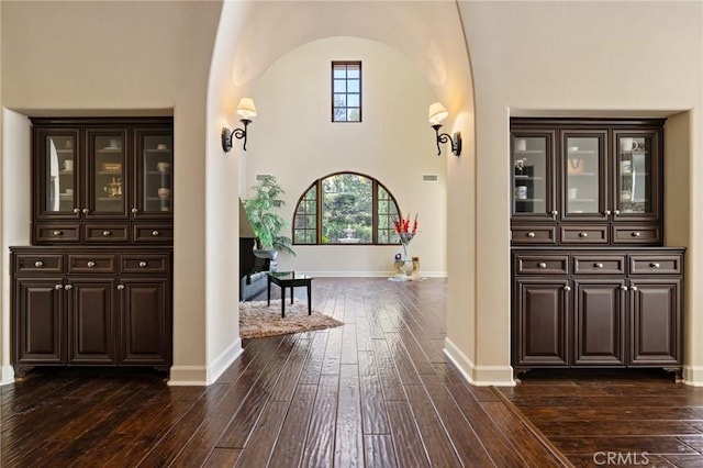 corridor with arched walkways, baseboards, and dark wood-style floors